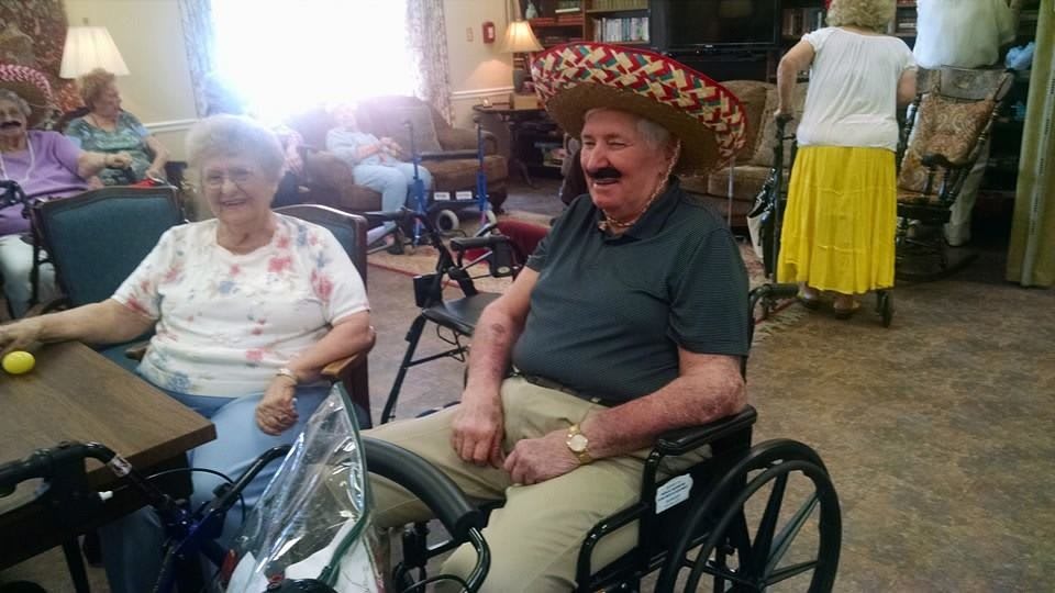 An elderly man in a wheelchair wearing a sombrero, enjoying a festive gathering.
