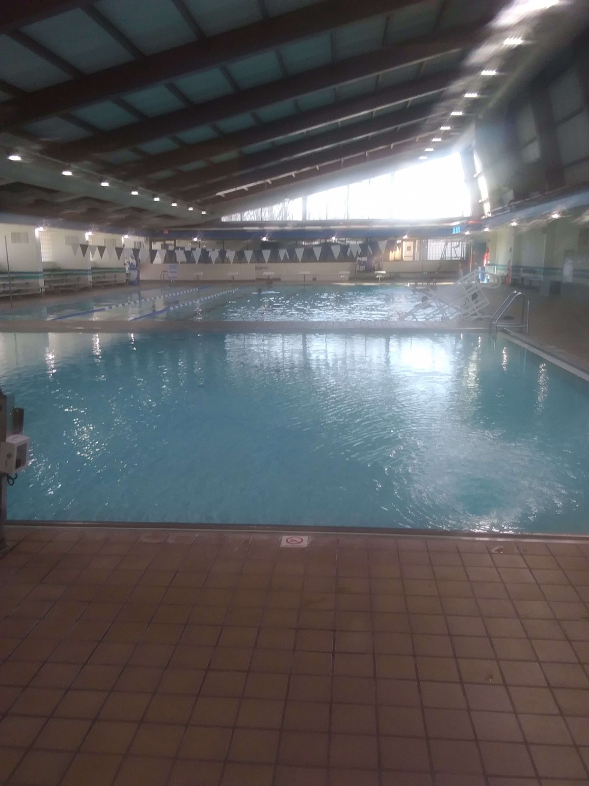 An indoor swimming pool with clean water, tile flooring, and overhead lighting.