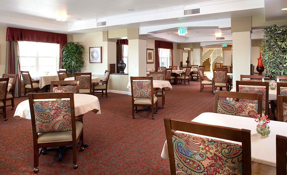 A spacious and well-lit dining area with tables and chairs arranged neatly, featuring patterned upholstery and elegant decor.