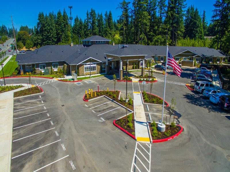 Aerial view of a modern building with a parking lot and landscaped entrance surrounded by trees.