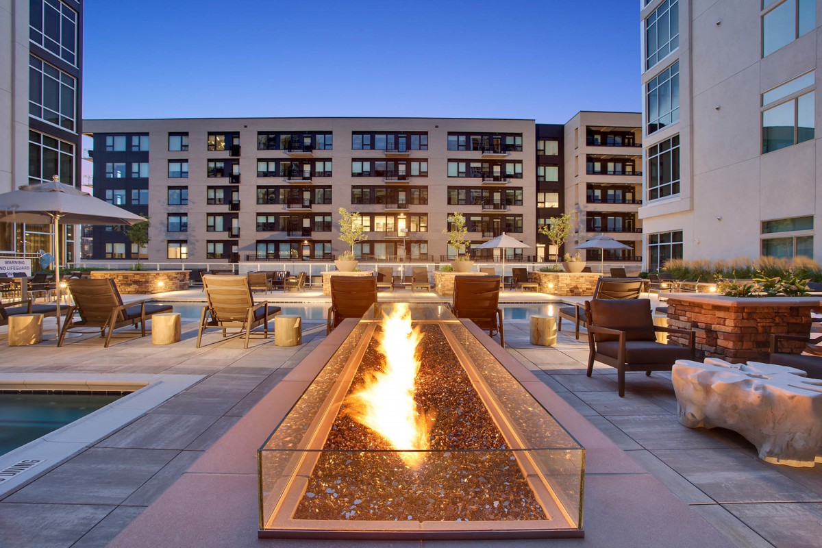 A cozy outdoor fire pit with seating in front of a modern apartment building at dusk.