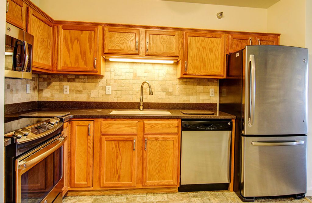 A modern kitchen featuring wooden cabinets, stainless steel appliances, and a stone countertop.