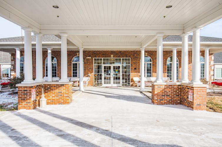 Entrance of a brick building with white columns and large windows.