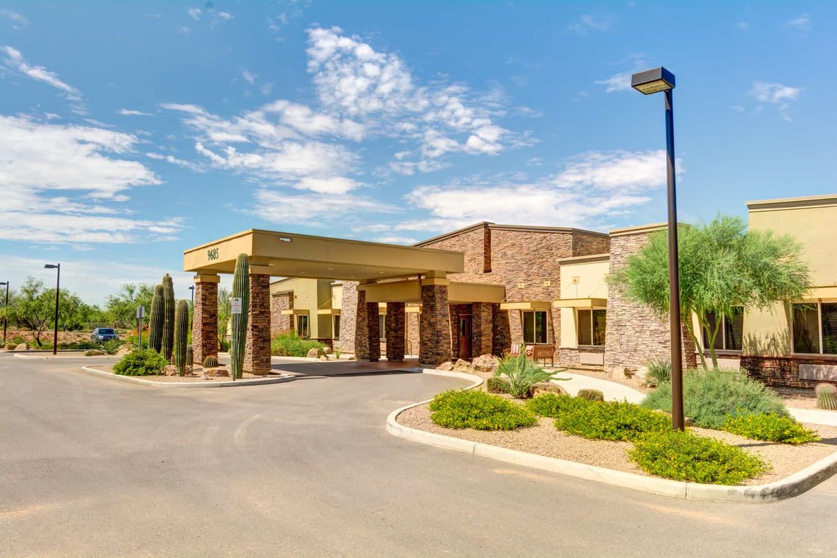 A modern building with a covered entrance and landscaped surroundings under a clear blue sky.
