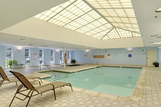 A serene indoor swimming pool area with lounge chairs under a skylight.