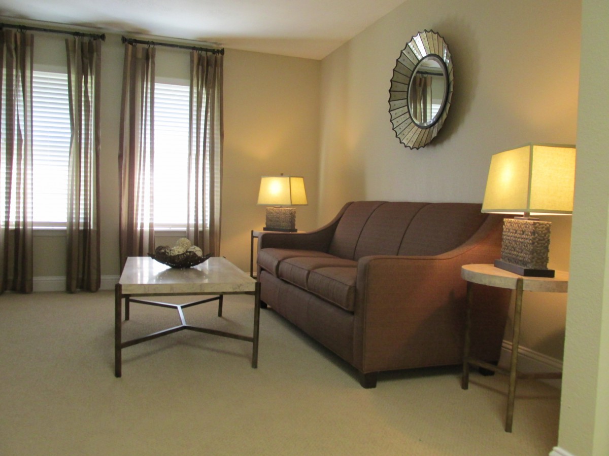 A well-lit living room featuring a brown sofa, two lamps, and a decorative mirror.