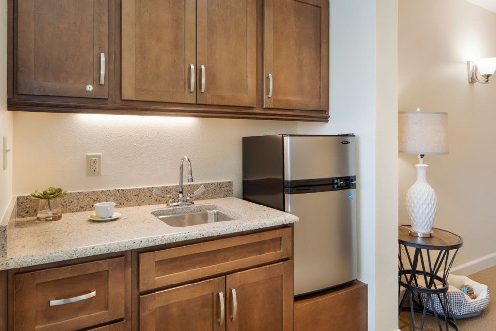 A compact kitchen area with wooden cabinets, a small sink, and a stainless steel fridge.