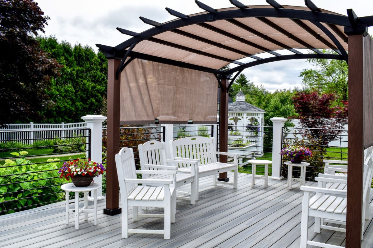A cozy outdoor patio area with a pergola and white seating arrangements, surrounded by plants and flowers.