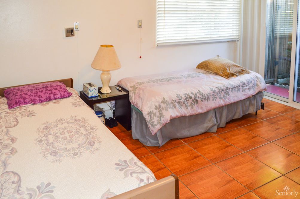 A cozy bedroom with two beds, a lamp on a side table, and wooden flooring.