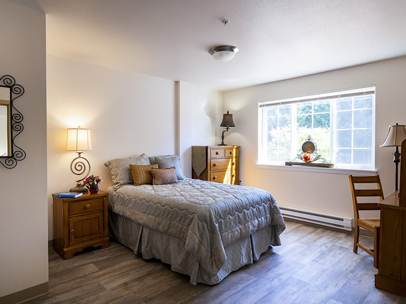 A cozy bedroom with a bed, side table, and chest of drawers illuminated by natural light from the window.