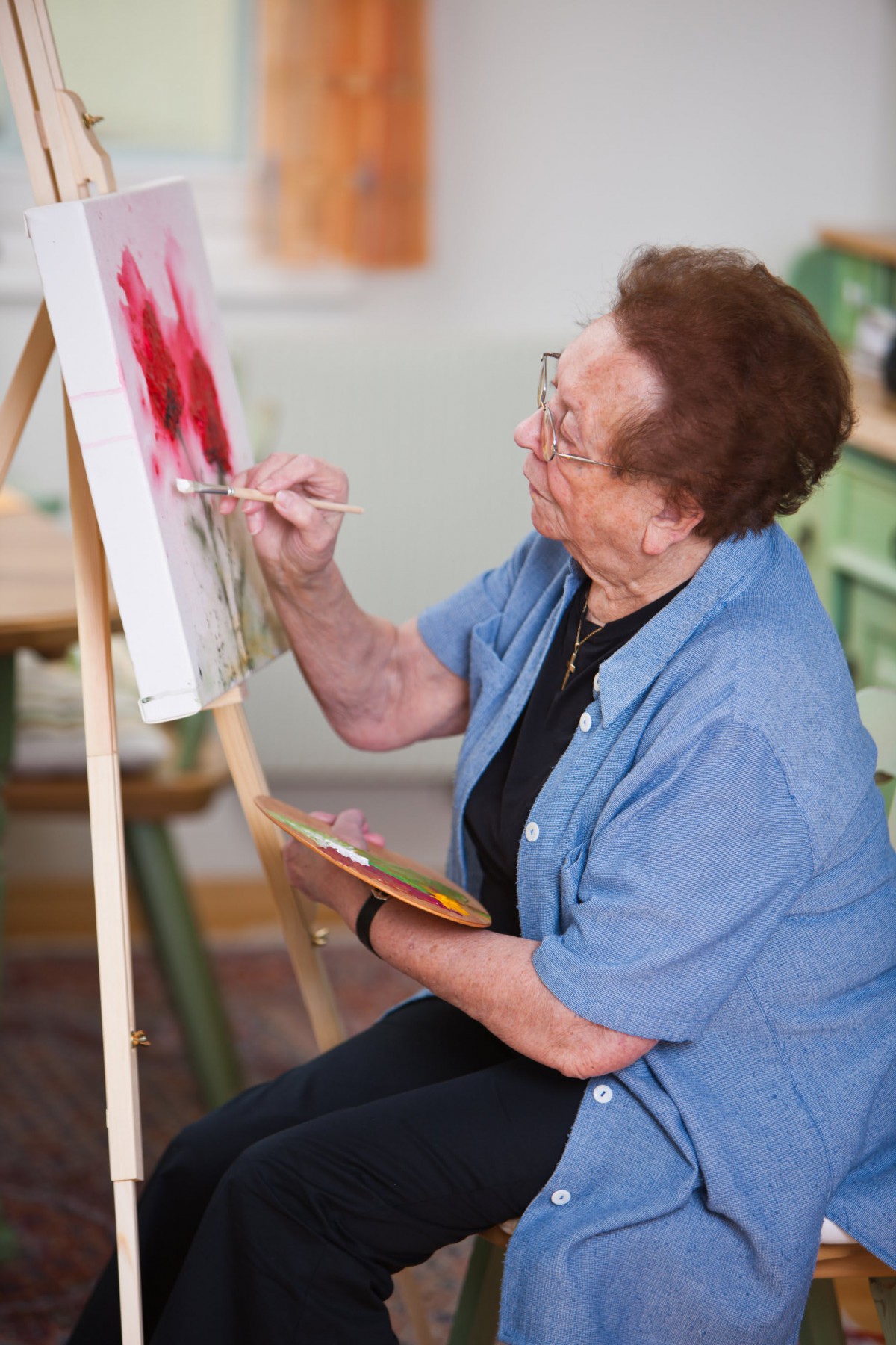 An elderly woman painting on a canvas in an art studio.