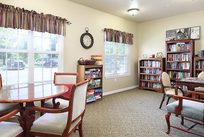 A cozy living room with a table and chairs, bookshelves, and large windows.
