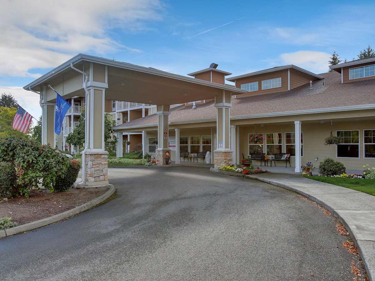 The image depicts the entrance of a residential building with a covered driveway and columns.