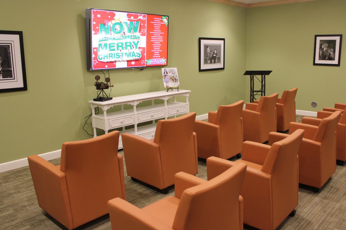 A cozy waiting room with orange chairs, a large screen for presentations, and a green accent wall.