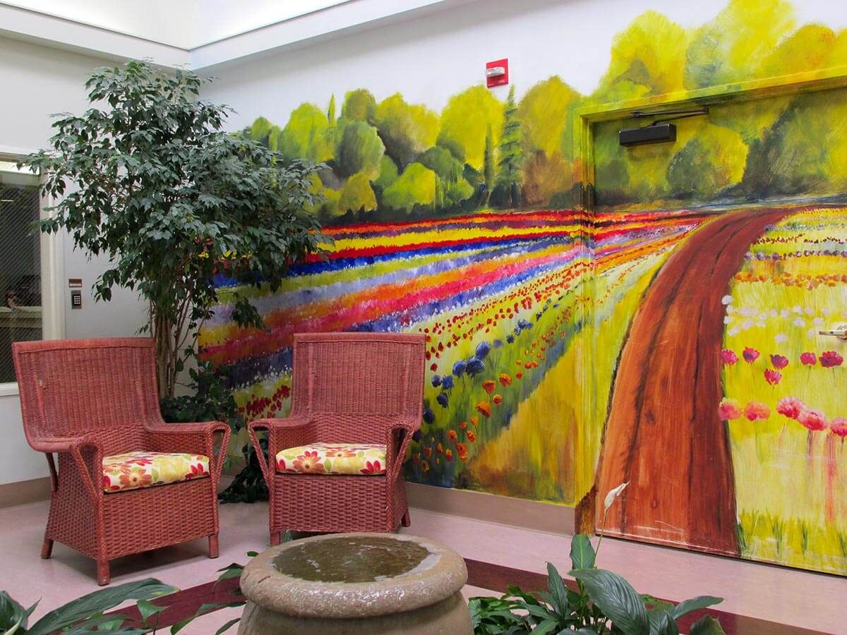 An indoor seating area featuring a vibrant mural of a scenic landscape with colorful fields and trees.