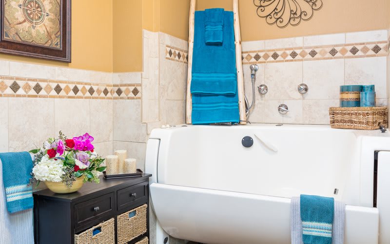 A cozy bathroom with a white bathtub, neatly folded blue towels, decorative candles, and wicker storage baskets.