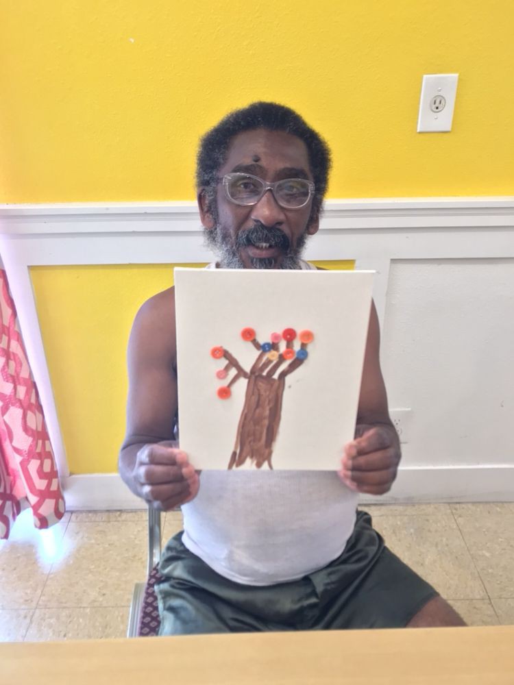 A man holding up a drawing of a tree with red leaves.