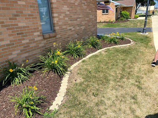 A well-maintained garden featuring a curved mulch border and blooming flowers next to a brick wall.