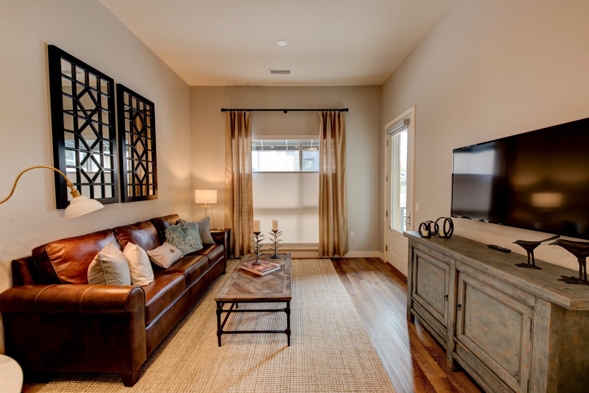 A modern living room with a comfortable sofa, stylish coffee table, and a television, featuring wood flooring and elegant curtains.