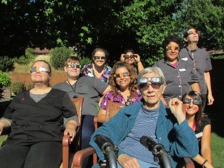 A group of people sitting outdoors wearing eclipse glasses to view a solar event.