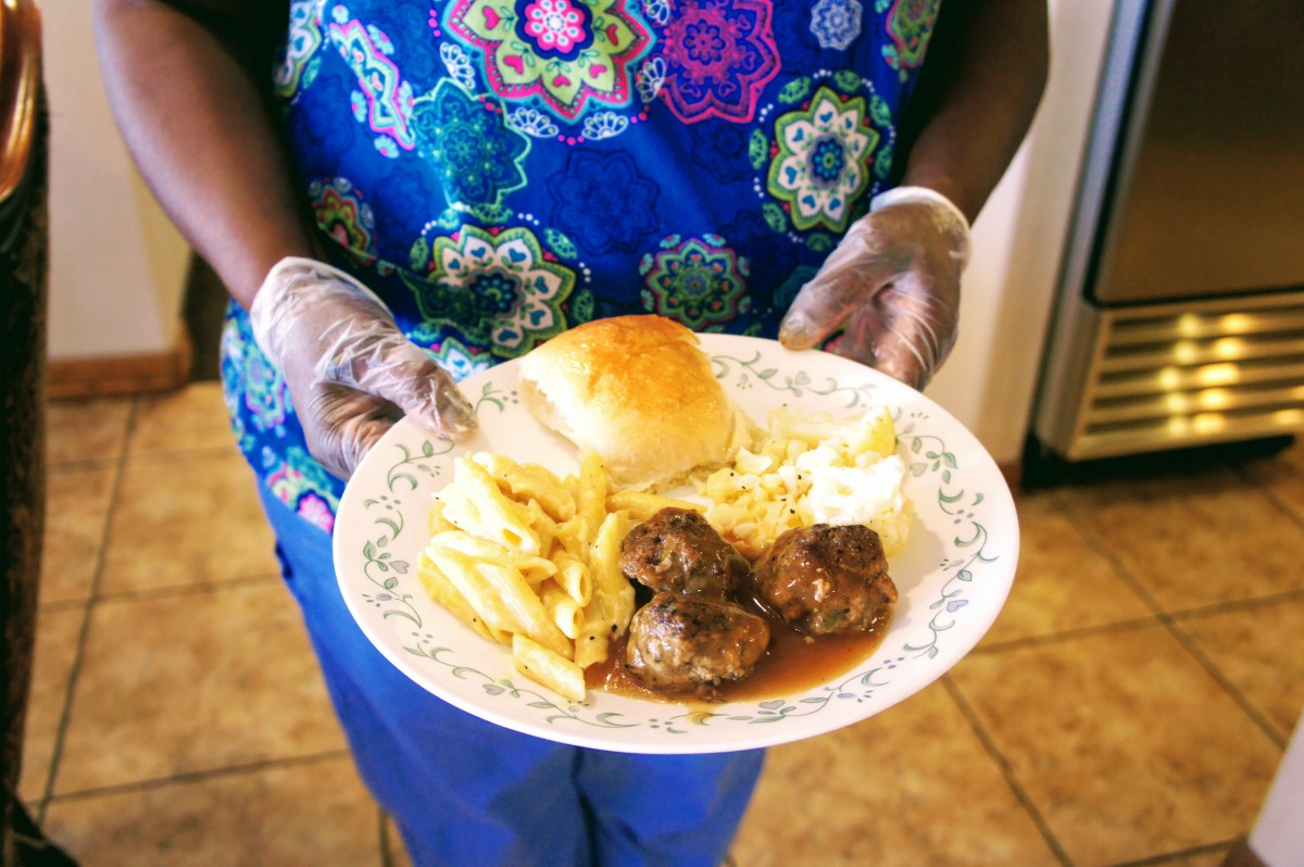 A person holding a plate with meatballs, fries, mashed potatoes, and a bread roll.