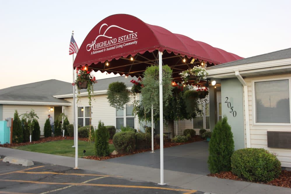 A building entrance with a red awning and decorative plants.