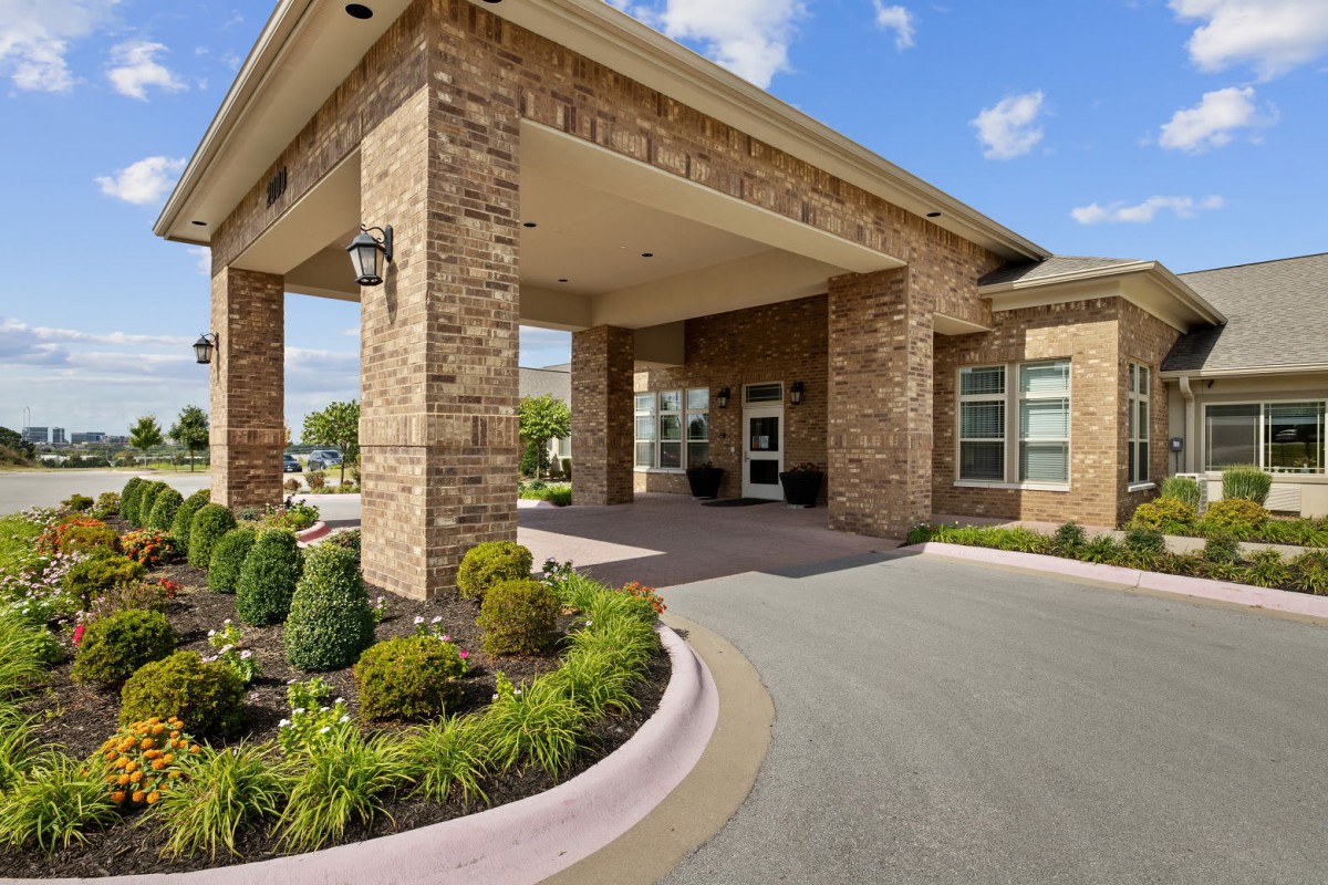 A brick building entrance with well-maintained landscaping and a driveway.
