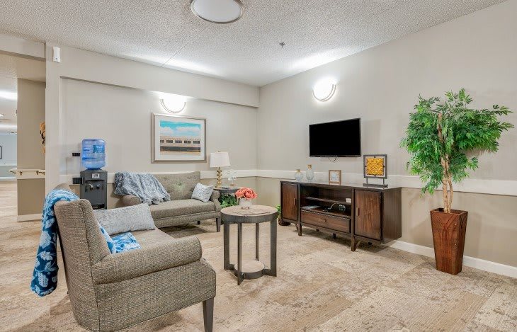 A cozy living room with a comfortable sofa, a wall-mounted television, artwork, and a coffee table on a carpeted floor.
