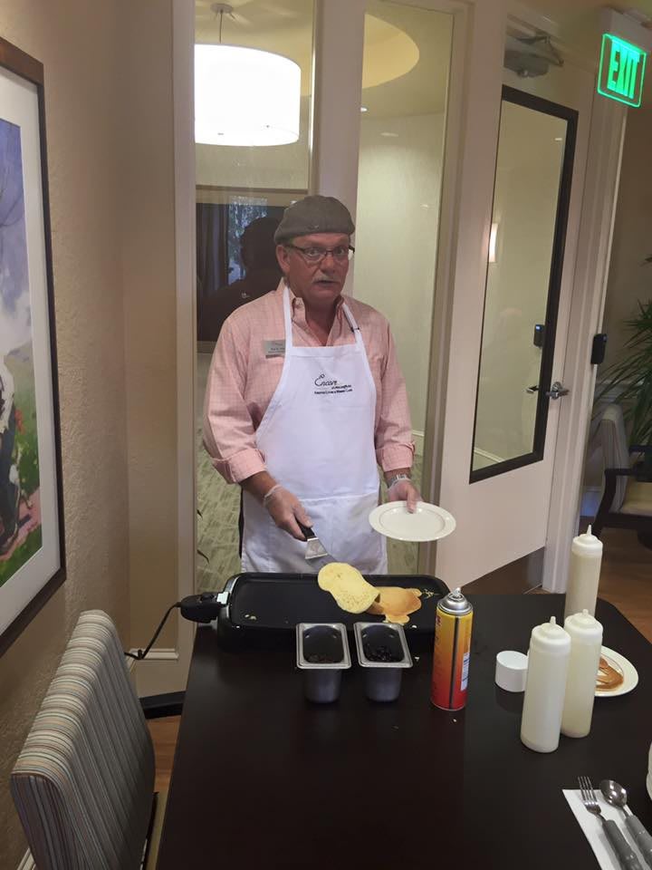A person cooking pancakes on a griddle while wearing an apron indoors.