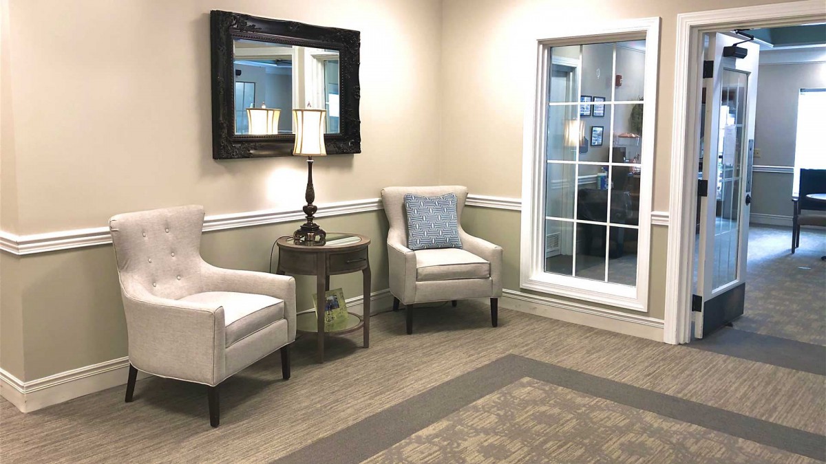 A cozy lobby with two chairs, a side table, and a lamp beneath a wall mirror.