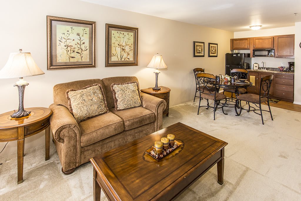 A cozy living room featuring a sofa, wooden coffee table, and artwork on the walls, with a dining area in the background.