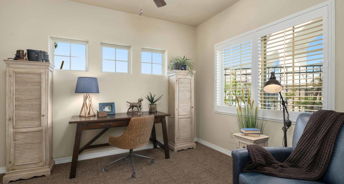A cozy home office with a desk, chair, and natural light from the windows.