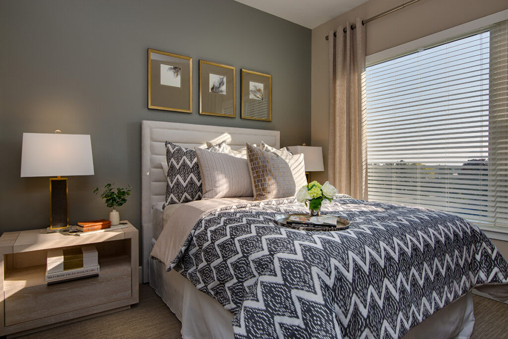 A modern and cozy bedroom with stylish zigzag-patterned bedding, complemented by soft lighting from a bedside lamp and natural light streaming through the window.