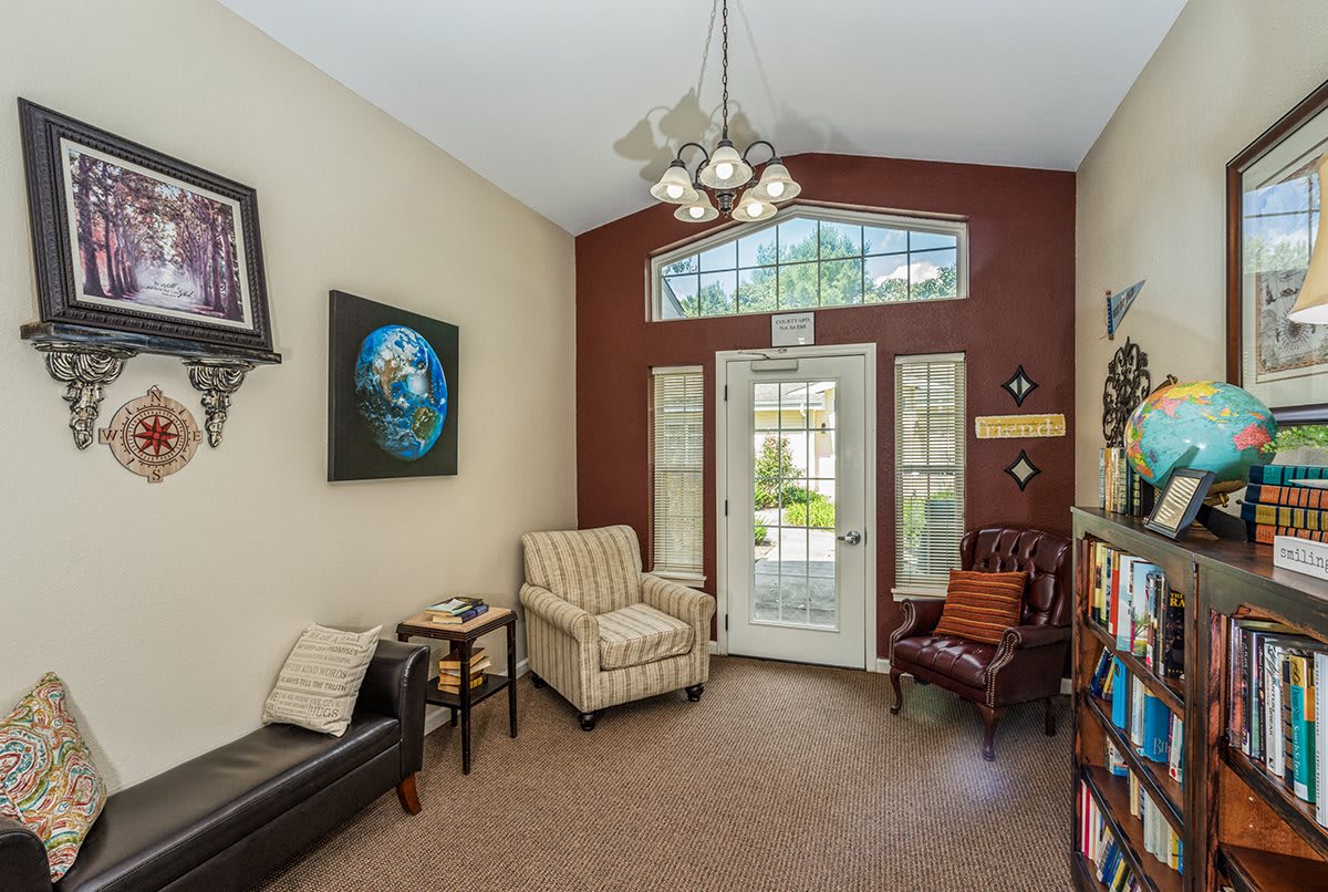 A cozy living room with comfortable chairs, a couch, and artwork on the walls. A large window lets in natural light.