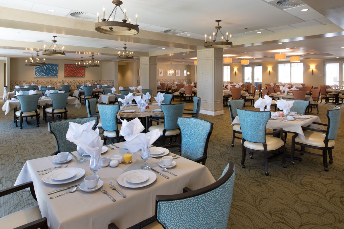 An elegantly set dining room with neatly arranged tables and chairs, featuring chandeliers and tasteful decor.