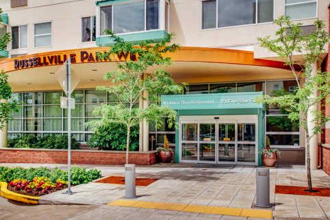 The entrance to a modern building with glass doors and surrounding greenery.