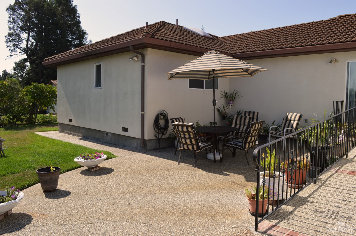 A sunny backyard patio with outdoor furniture and an umbrella.