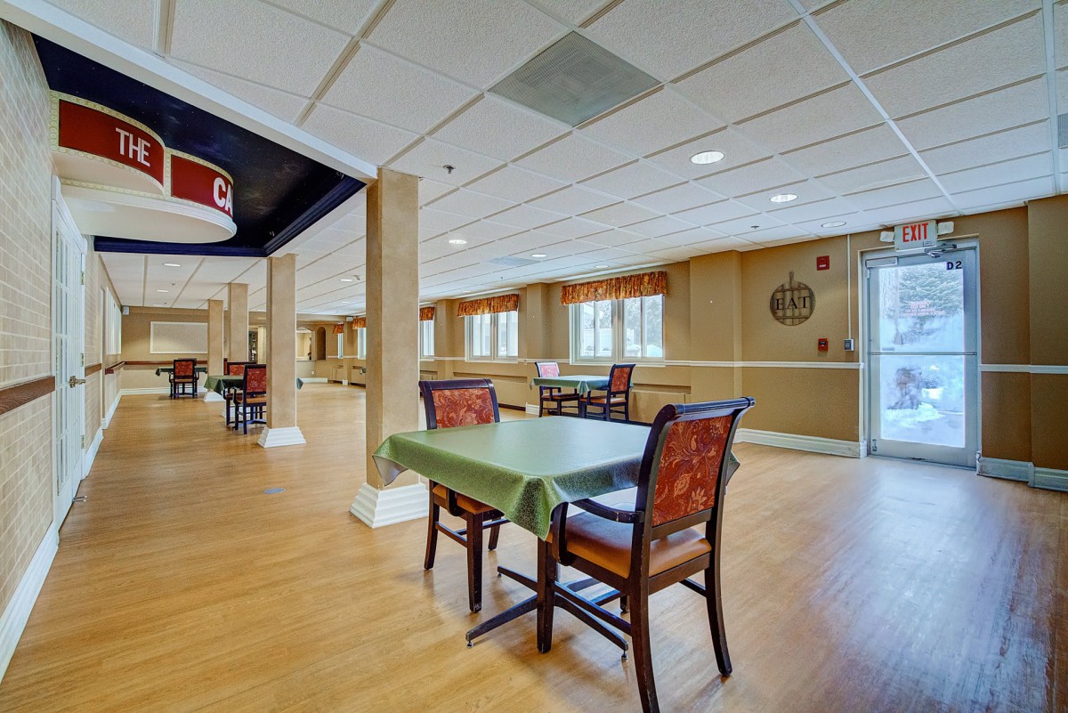 An empty dining area with neatly arranged tables and chairs, featuring a wooden floor and ample natural light from the windows.