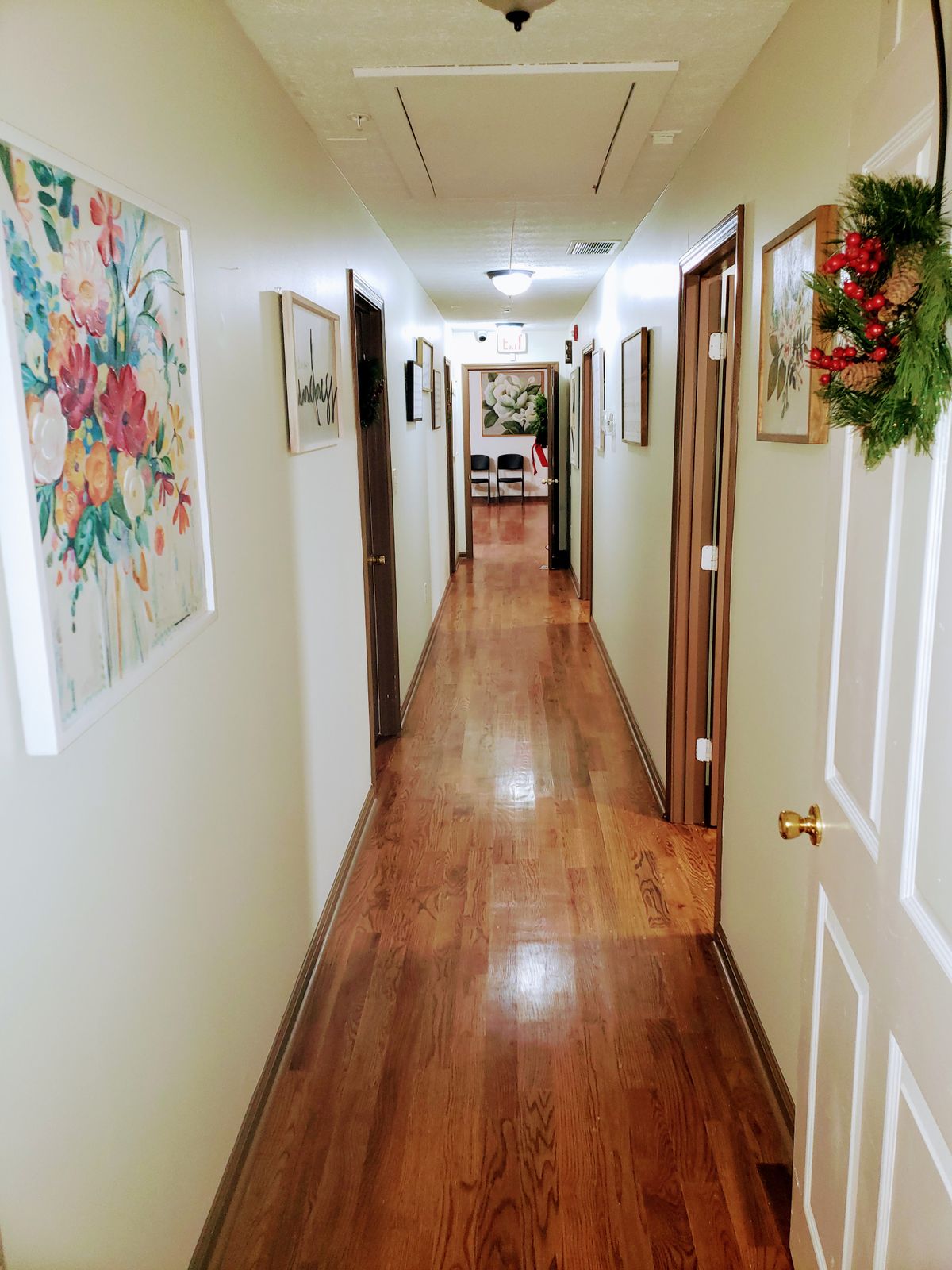 A long indoor hallway with a wooden floor, adorned with framed artwork and doors on either side.