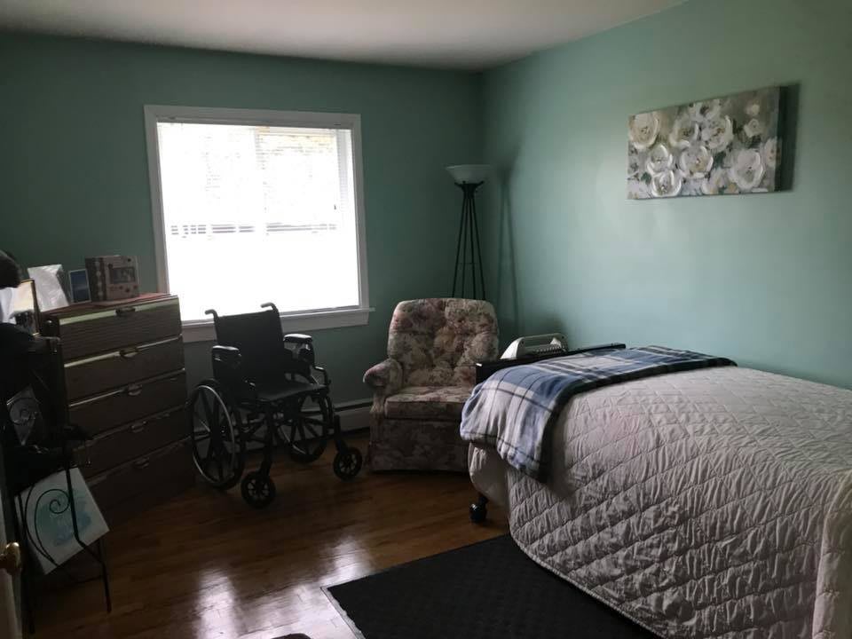 A cozy bedroom with a bed, armchair, and wheelchair by the window.