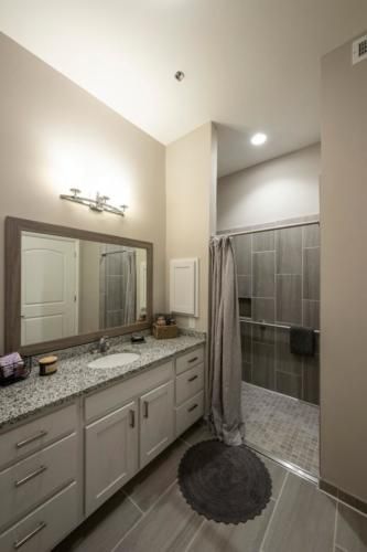 A modern bathroom with a granite countertop, large mirror, and walk-in shower.