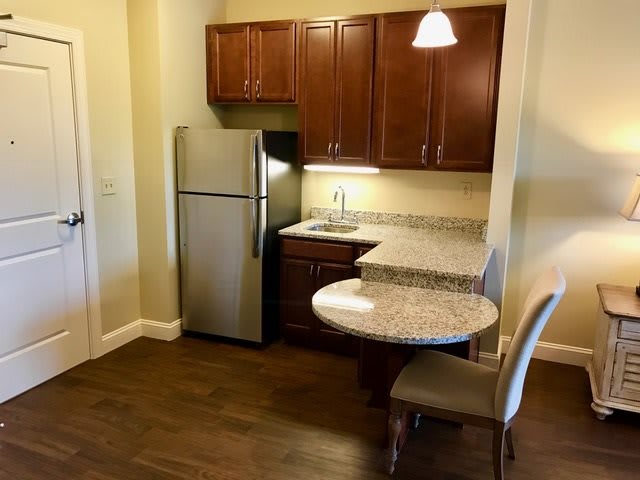 A compact apartment kitchen with stainless steel appliances and wooden cabinets.