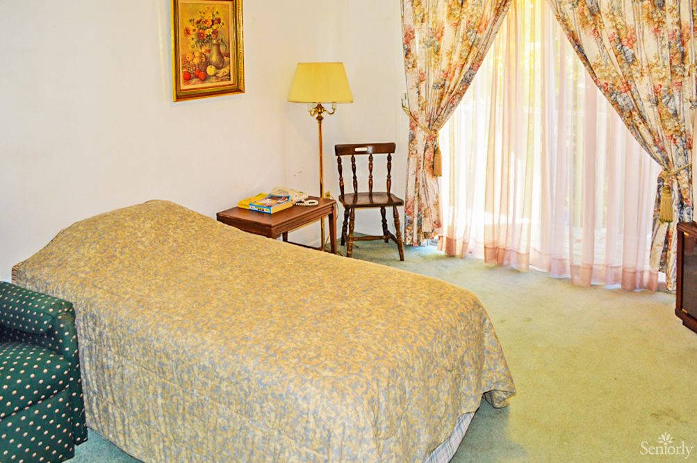 A cozy bedroom with a single bed, lamp, and elegant curtains.