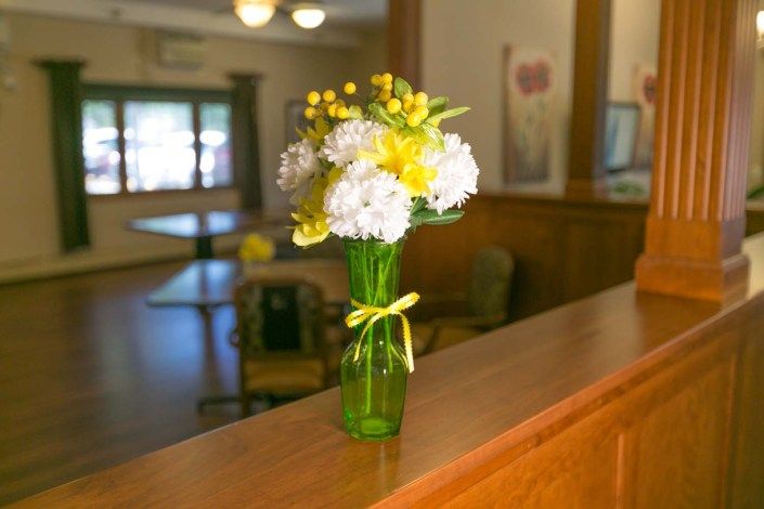 A bouquet of white and yellow flowers in a green vase placed on a wooden ledge inside a room.
