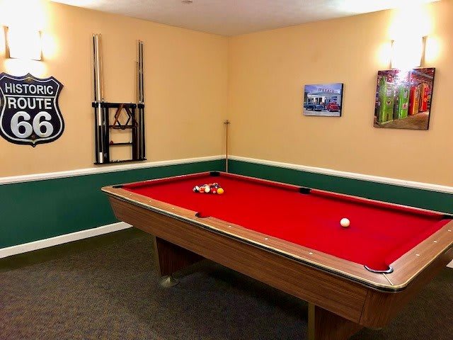 A cozy game room featuring a pool table with red felt, a guitar mounted on the wall, and framed pictures.