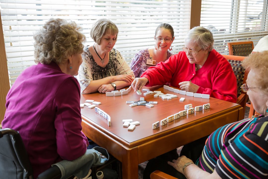 A group of seniors playing dominoes together at a table indoors.