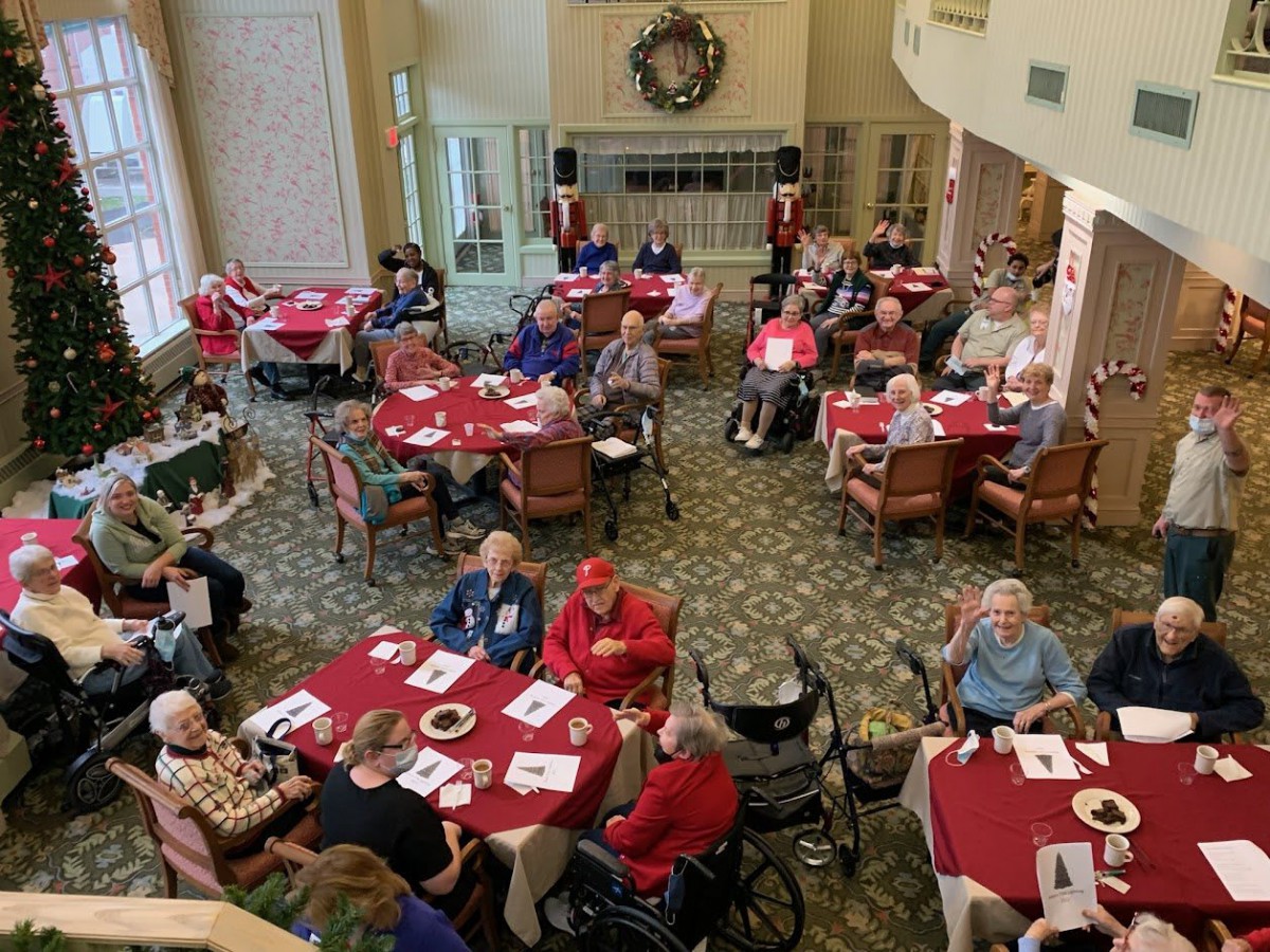 A community gathering of seniors enjoying a social event indoors with tables covered in red tablecloths.