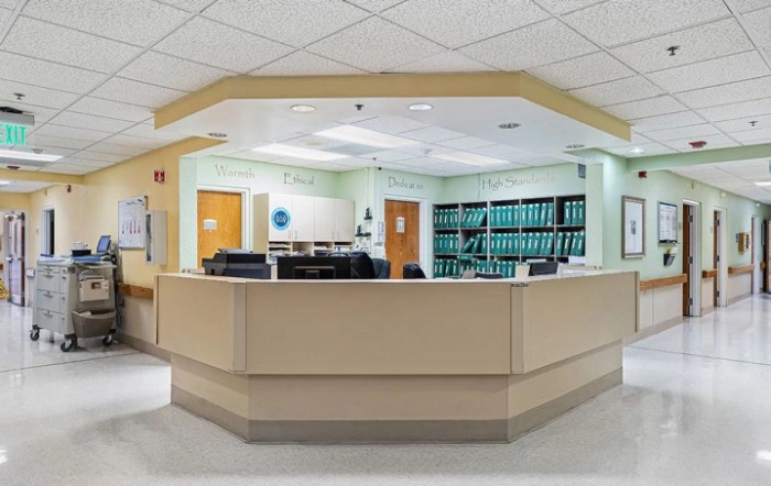 A hospital reception area with a central desk and shelves in the background.