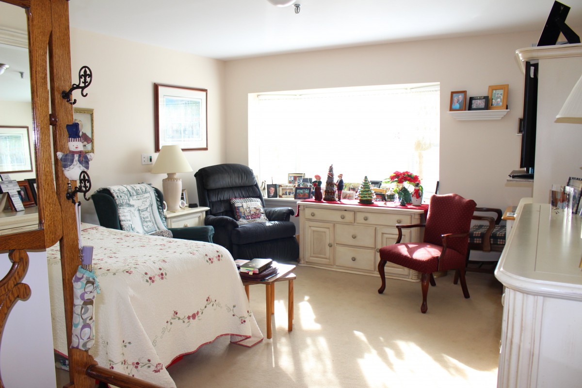 A cozy living room setup with a bed, chairs, and decorations by a large window.