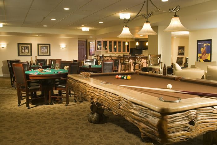 A cozy and well-lit game room featuring a rustic pool table, surrounded by comfortable furniture and ambient lighting.